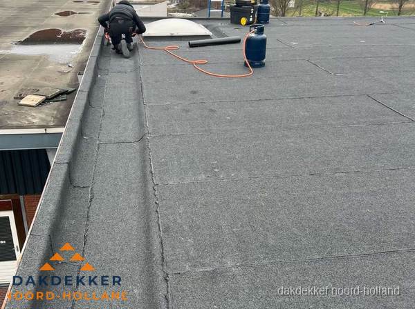 Dakdekker repareert bitumen dakbedekking op groot plat dak in Noord-Holland