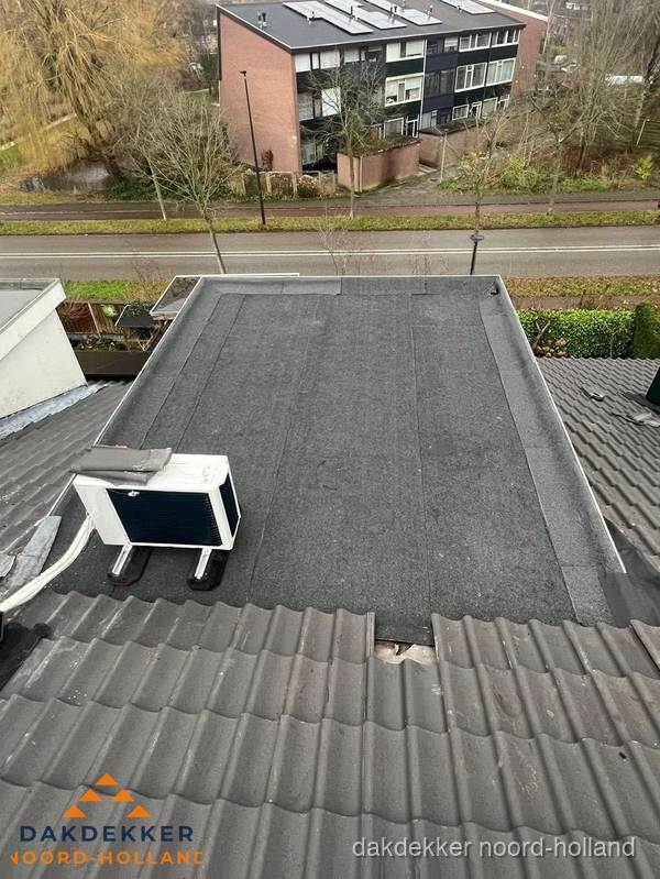 Plat dak inspectie met bitumen bedekking naast schuin pannendak in Noord-Holland