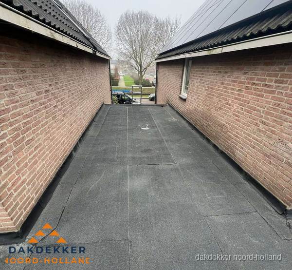 Plat dak met bitumen dakbedekking tussen bakstenen muren in Noord-Holland